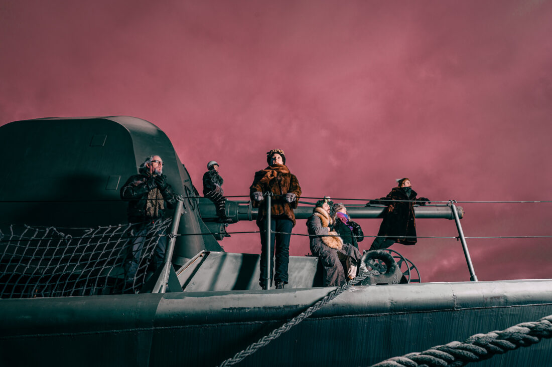 Kuvassa viisi henkilöä sotalaivan kannella.